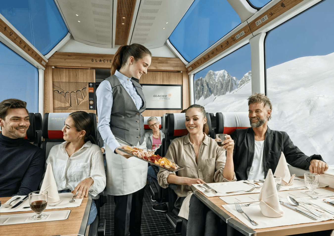 Das Bild zeigt ein luxuriöses Zug-Dining-Erlebnis, bei dem Passagiere die Aussicht auf die Berge genießen.