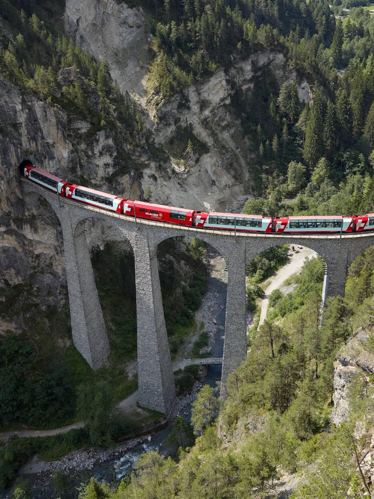 La photo montre un train Glacier Express passant sur un pont.