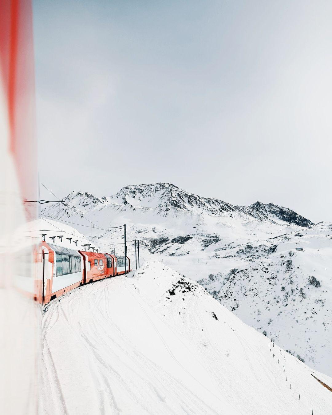 Auf dem Bild ist zu sehen, wie der Glacier Express durch eine verschneite Berglandschaft fährt