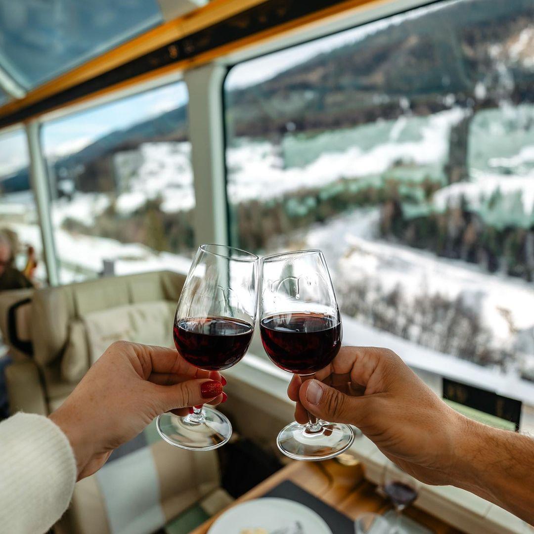 Auf dem Bild ist zu sehen, wie zwei Gläser Rotwein im Glacier Express zum Anstoßen erhoben werden