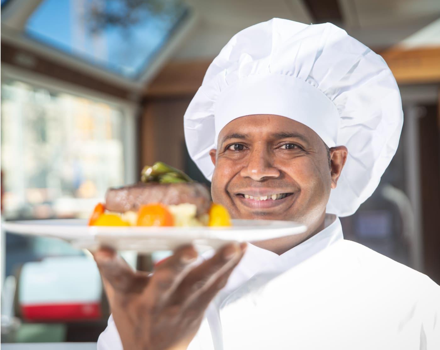 The image shows a smiling chef holding a plate of food.